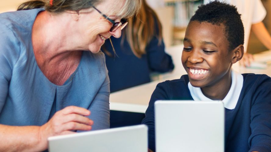 Teacher sat with student holding a tablet computer.